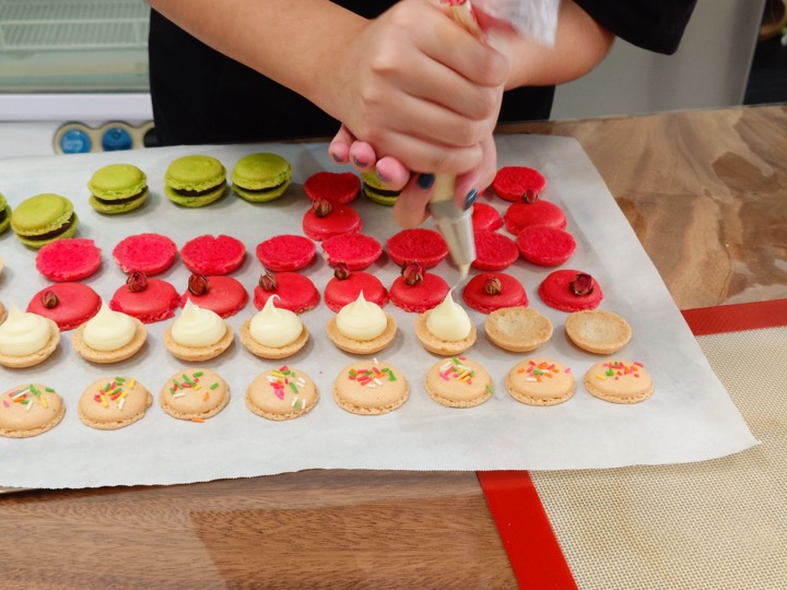 Piping cream filling onto colourful macaron shells at the studio table